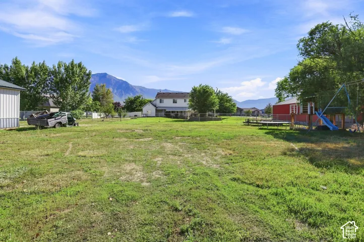 Expansive grassy yard with mountain scenery, surrounded by mature trees, featuring a red shed