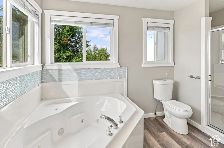 Corner soaking tub with polished chrome fixtures, glass mosaic tile surround, and wood-finish flooring