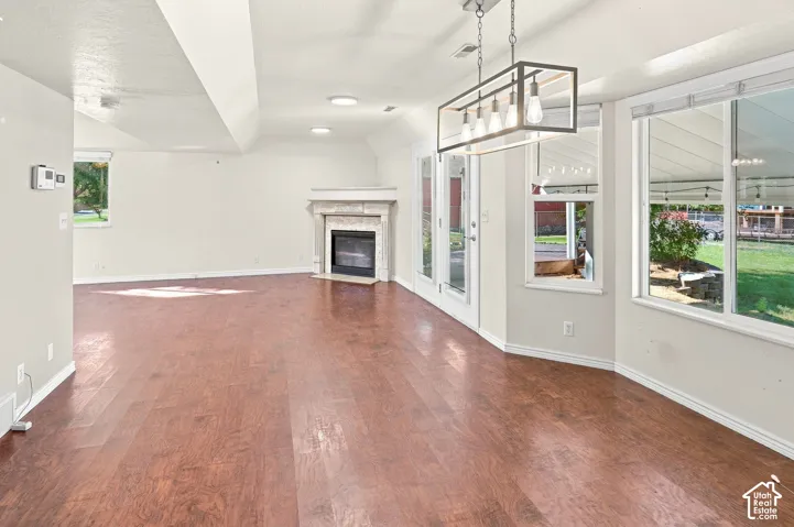 Wood-finish flooring throughout, featuring a corner fireplace with a stone surround, recessed lighting, and a modern rectangular chandelier