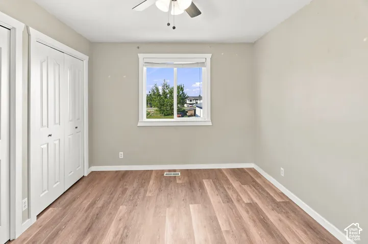 Wood-finish flooring with white trim, a double bi-fold closet, and a ceiling fan