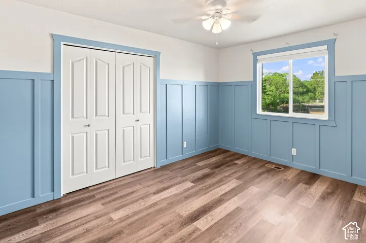 Wood-finish flooring, accent wall with wainscoting, white bi-fold closet doors, and a ceiling fan