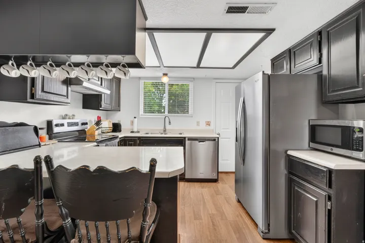 Wood-finish flooring with stainless steel appliances, dark cabinetry, and light countertops