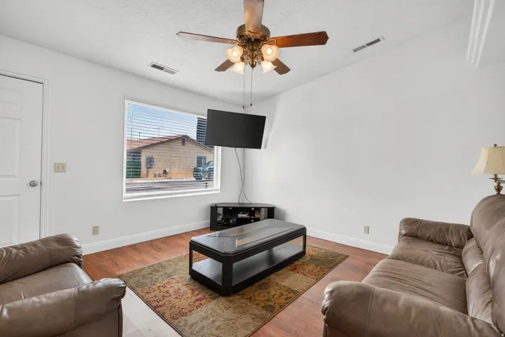 Vaulted ceiling with a ceiling fan light fixture, wood-finish flooring, white walls, and a window with horizontal blinds