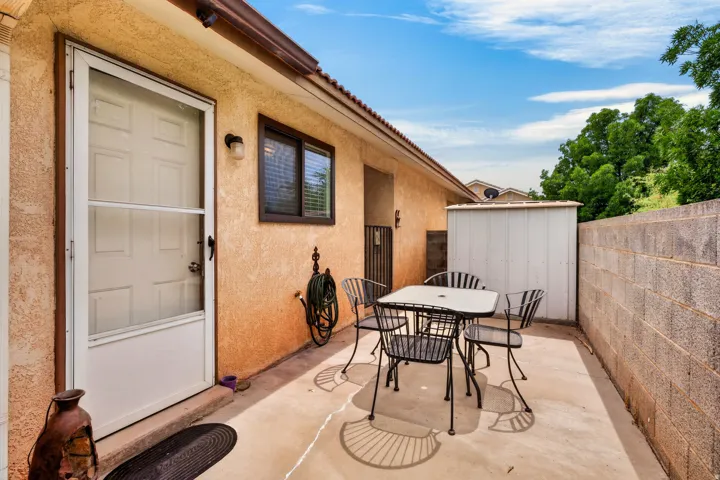 Paved concrete patio featuring a block wall, exterior lighting, an exterior door with a screen, and a storage shed