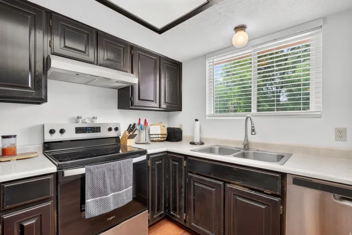 Kitchen featuring dark wood cabinetry, stainless steel appliances, a dual basin sink with a high-arc faucet, and light-toned countertops