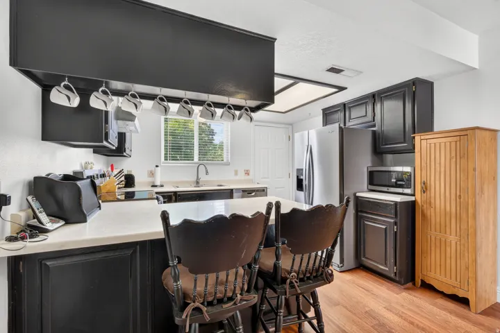 Kitchen featuring black cabinetry, stainless steel appliances, wood-finish flooring, and a window above the sink
