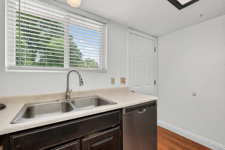 Stainless steel double basin sink with a pull-down faucet, light-toned countertop, dark wood-finish cabinetry, and stainless steel dishwasher