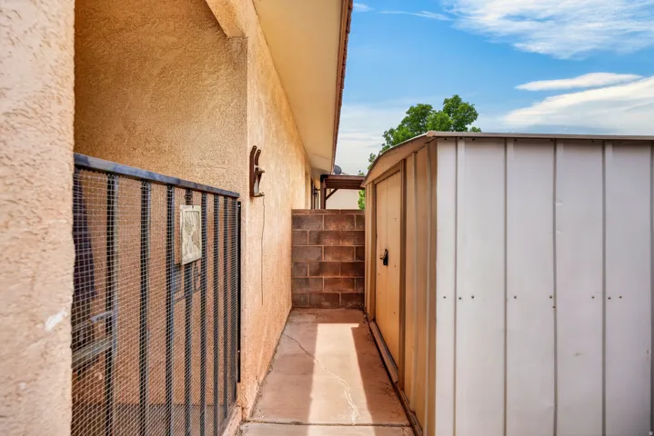 Exterior stucco wall, concrete pathway, metal storage shed, and a decorative metal gate