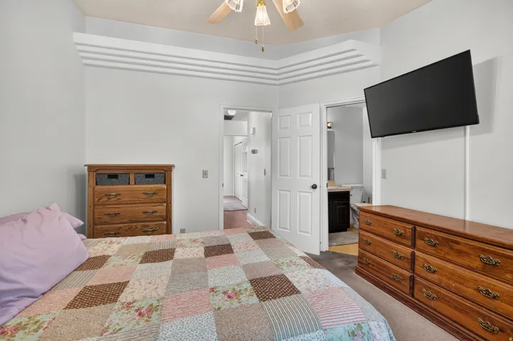 Tray ceiling with layered trim details, ceiling fan with light fixture, wall-mounted television, and carpeted flooring