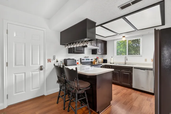 Kitchen featuring wood-finish flooring, dark wood cabinetry, light countertops, and a stainless steel dishwasher