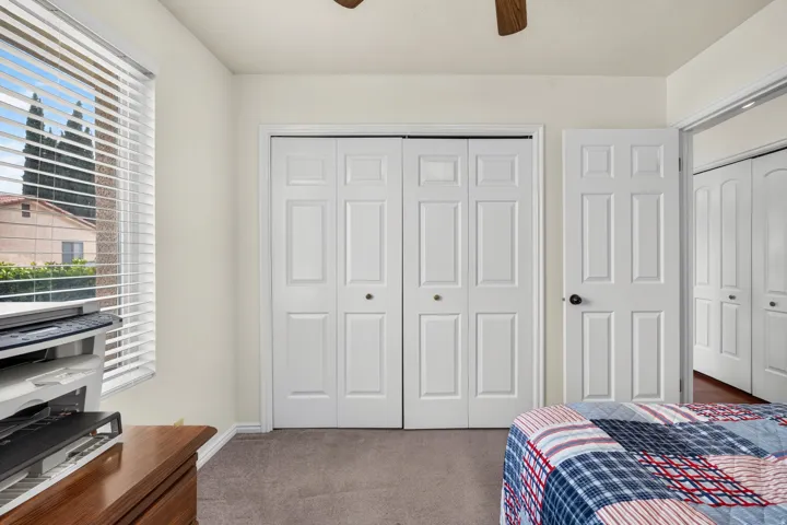 White bi-fold closet doors, neutral wall paint, white window blinds, and gray carpeting