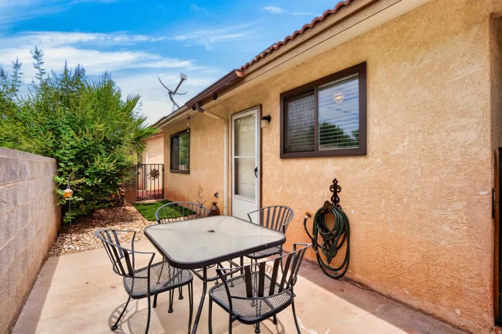 Private concrete patio with stucco exterior, a secure gate, and mature landscaping