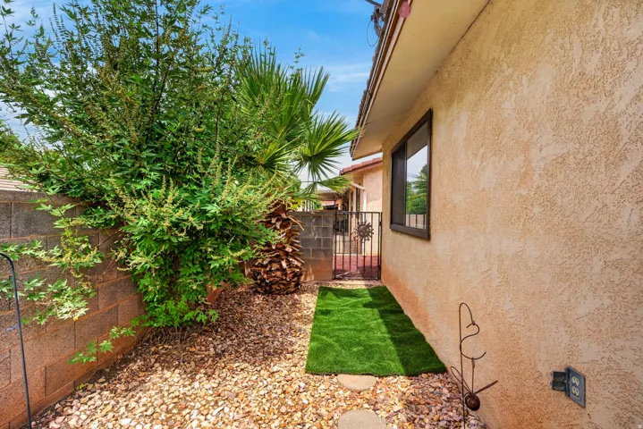 Stucco exterior with a dark-framed window, gravel landscaping, established shrubbery, and a decorative metal gate