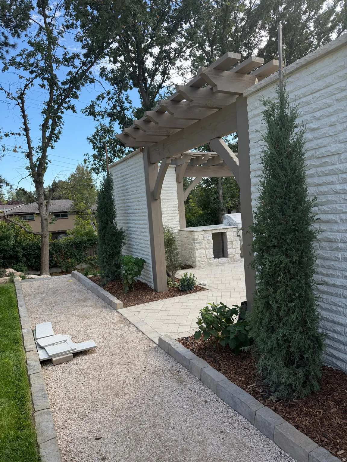 Pergola entryway with a stone-clad wall and paver patio