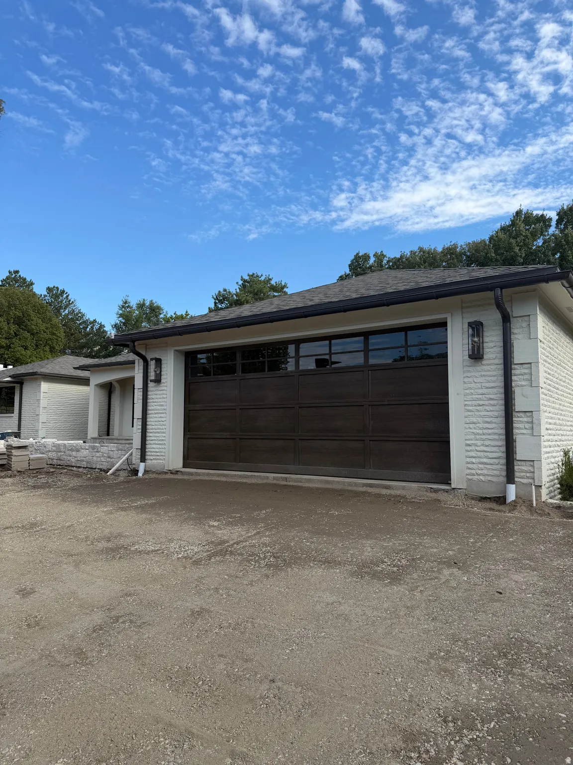 Contemporary overhead garage door with multiple window panels, complemented by exterior wall sconces and white brick siding