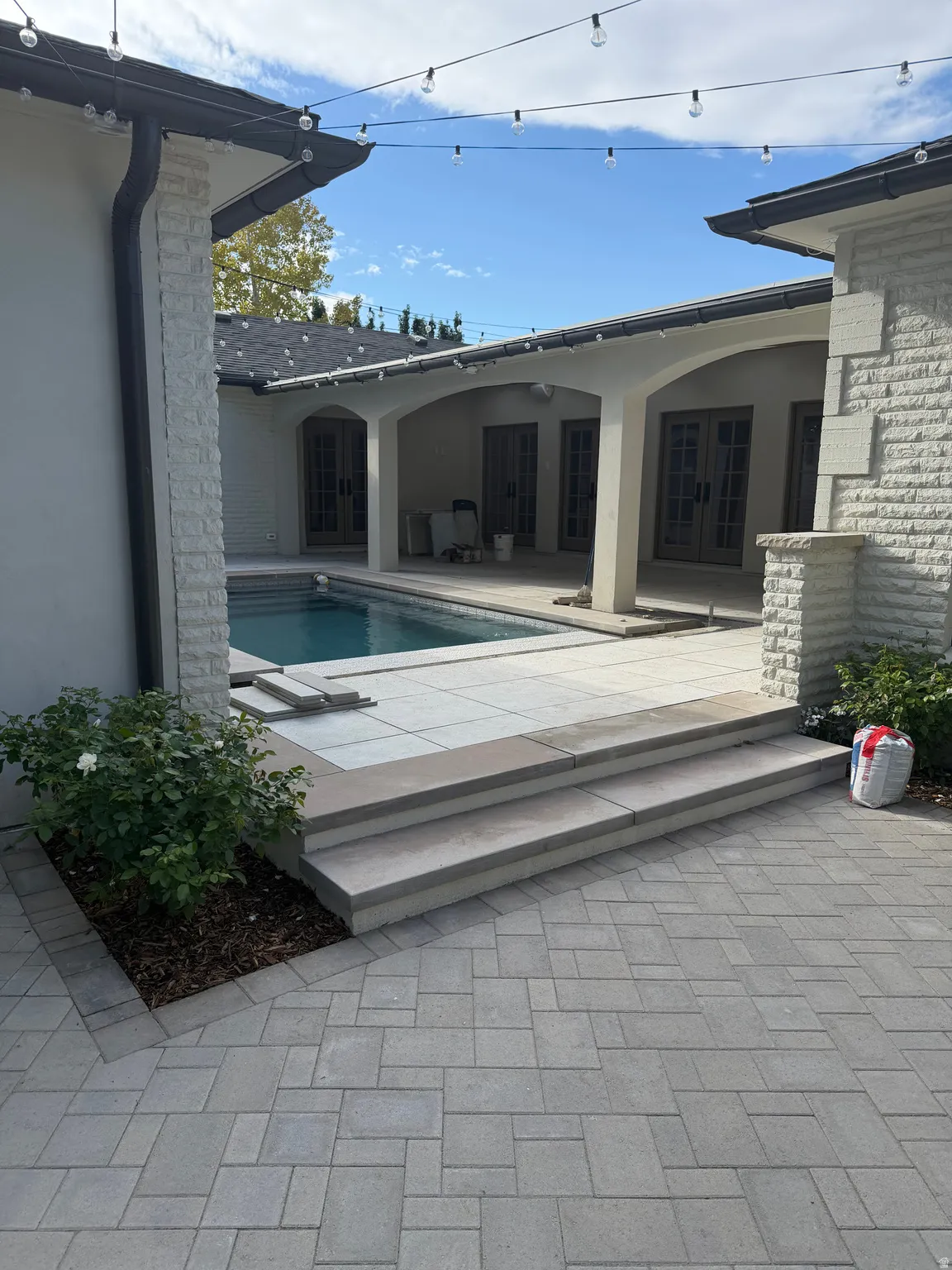 Outdoor paver patio with a stepped entry to the pool deck, surrounded by stucco and stone-clad architectural elements