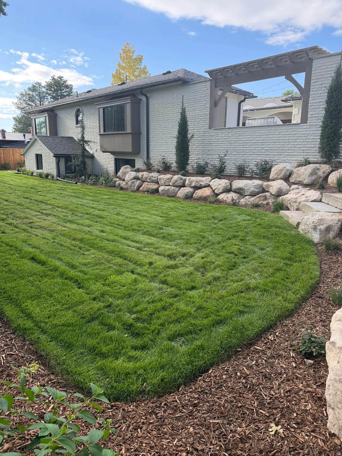 Expansive lawn with rock retaining wall, mature plantings, and a pergola structure
