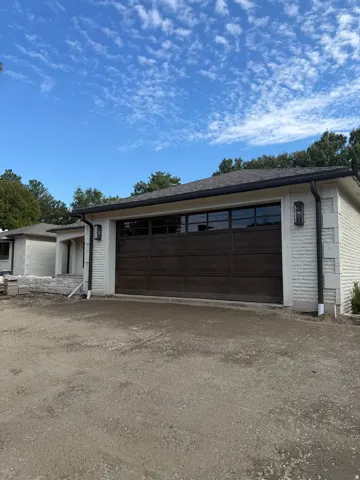 Contemporary overhead garage door with multiple window panels, complemented by exterior wall sconces and white brick siding