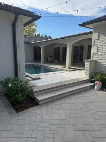 Outdoor paver patio with a stepped entry to the pool deck, surrounded by stucco and stone-clad architectural elements