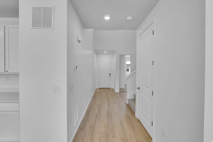 Long hallway with wood-finish flooring, recessed lighting, and a white paneled door