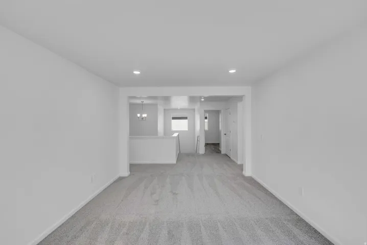 Recessed lighting, light gray carpet, white walls, white railing, and a chandelier in the background