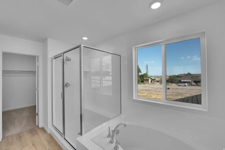 Glass-enclosed shower with a built-in bench, adjacent soaking tub with deck-mounted fixtures, and a window providing natural light