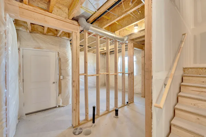 Unfinished interior space featuring exposed wood framing, rough-in plumbing, and a partially framed staircase with wood handrail