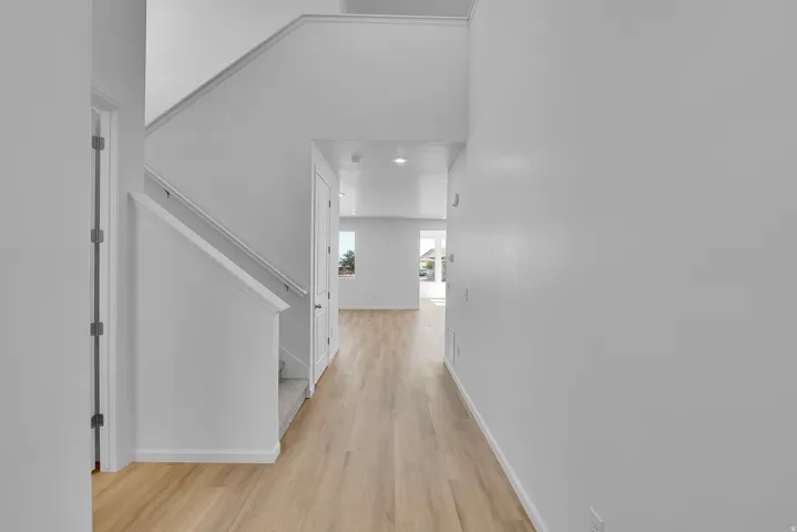 Hallway featuring wood-finish flooring, white walls, and a staircase with a white handrail