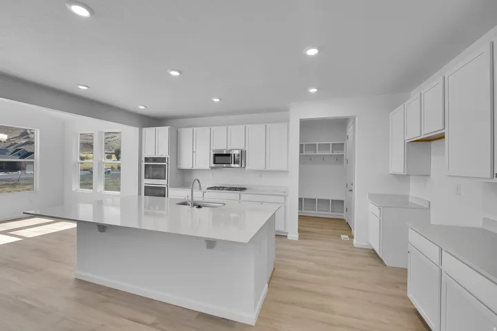 Spacious kitchen featuring an extended island with a sink, white cabinetry, integrated stainless steel appliances, and wood-finish flooring