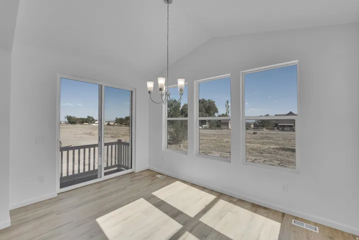 Vaulted ceiling, wood-finish flooring, sliding glass door, white walls, and a multi-light chandelier