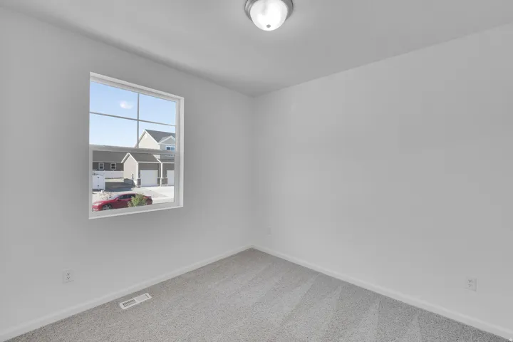 Neutral wall paint, ceiling-mounted light fixture, carpeted flooring, and a large window with grilles
