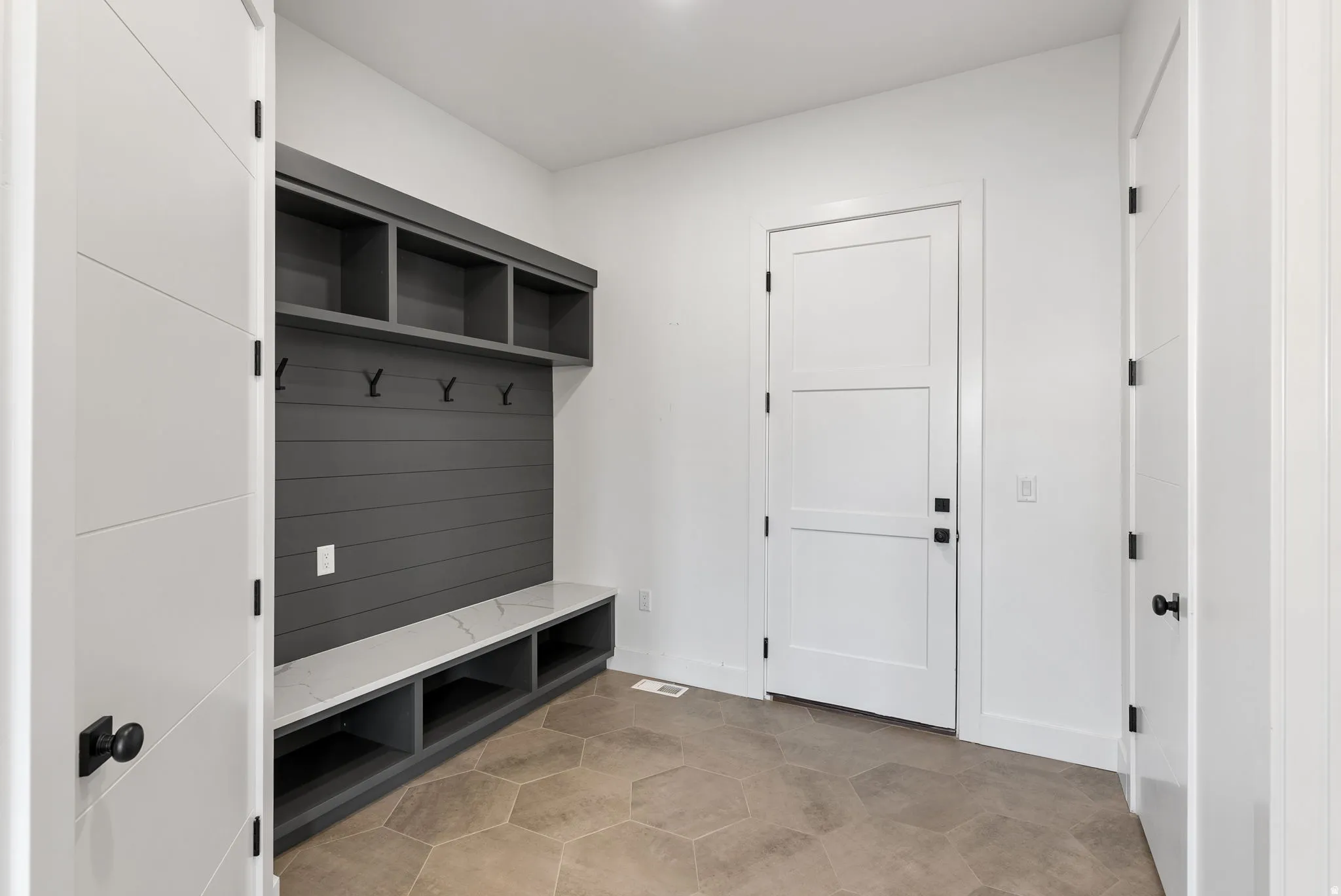 Built-in mudroom storage with slat wall, open shelving, and integrated bench with a light-toned countertop, complemented by hexagonal floor tiles