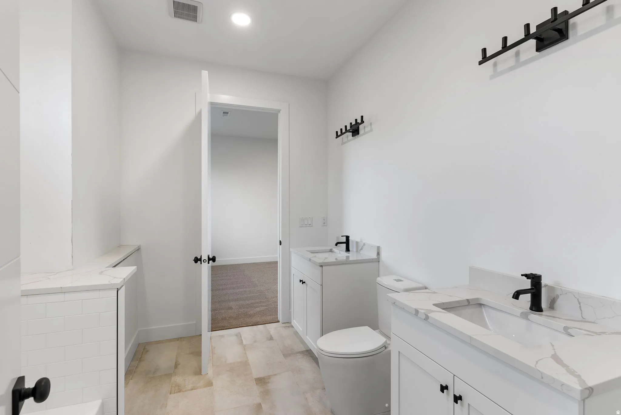 Dual white vanity cabinets with integrated sinks, light-toned tile flooring, and matte black fixtures