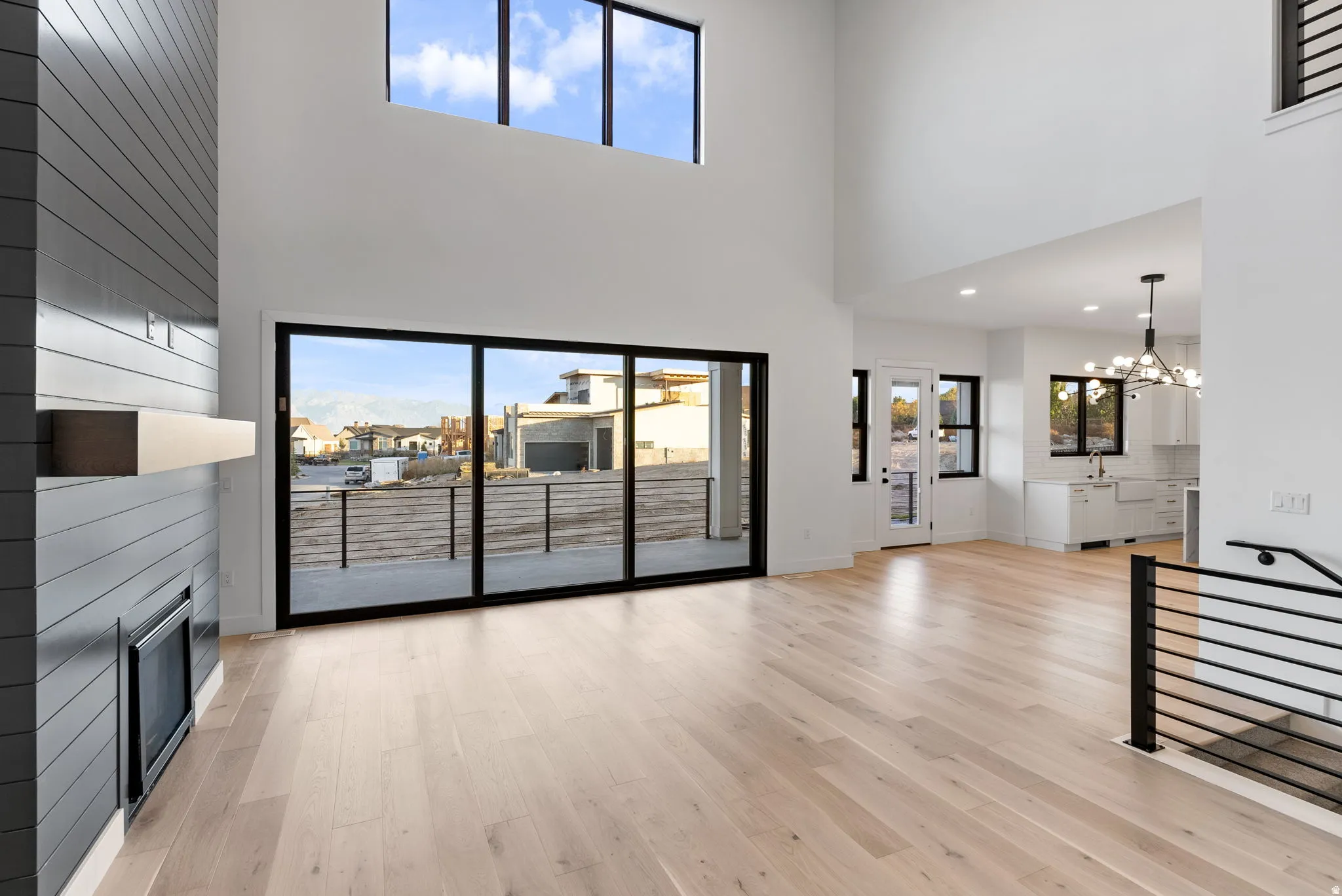 Spacious interior with high ceilings, light wood-finish flooring, a contemporary fireplace, large sliding glass doors, and a modern staircase railing