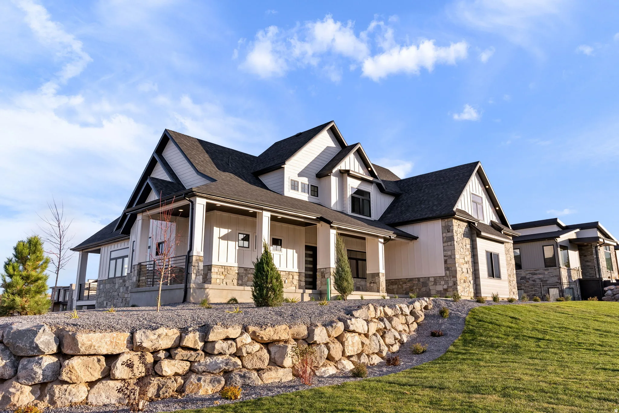 Modern farmhouse exterior with white vertical siding, dark trim, stone accents, covered front porch, and an asphalt shingle roof