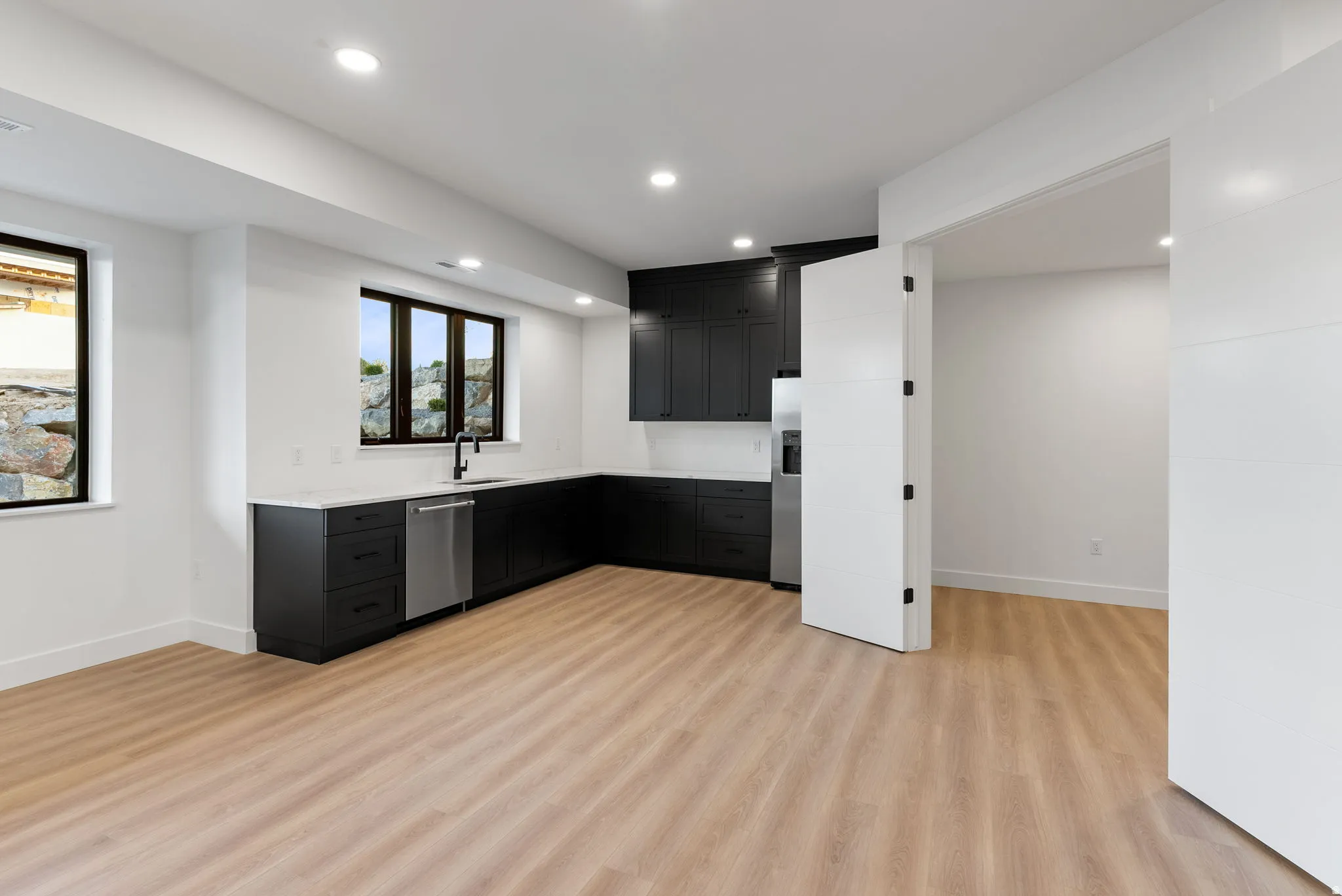 L-shaped cabinetry with matte black finishes, stainless steel dishwasher, undermount sink with a black faucet, recessed lighting, and wood-finish flooring