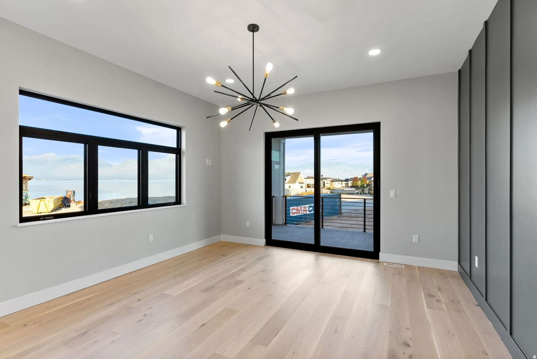 Light wood-finish flooring, a contemporary sputnik chandelier, recessed lighting, and a large window with water scenery