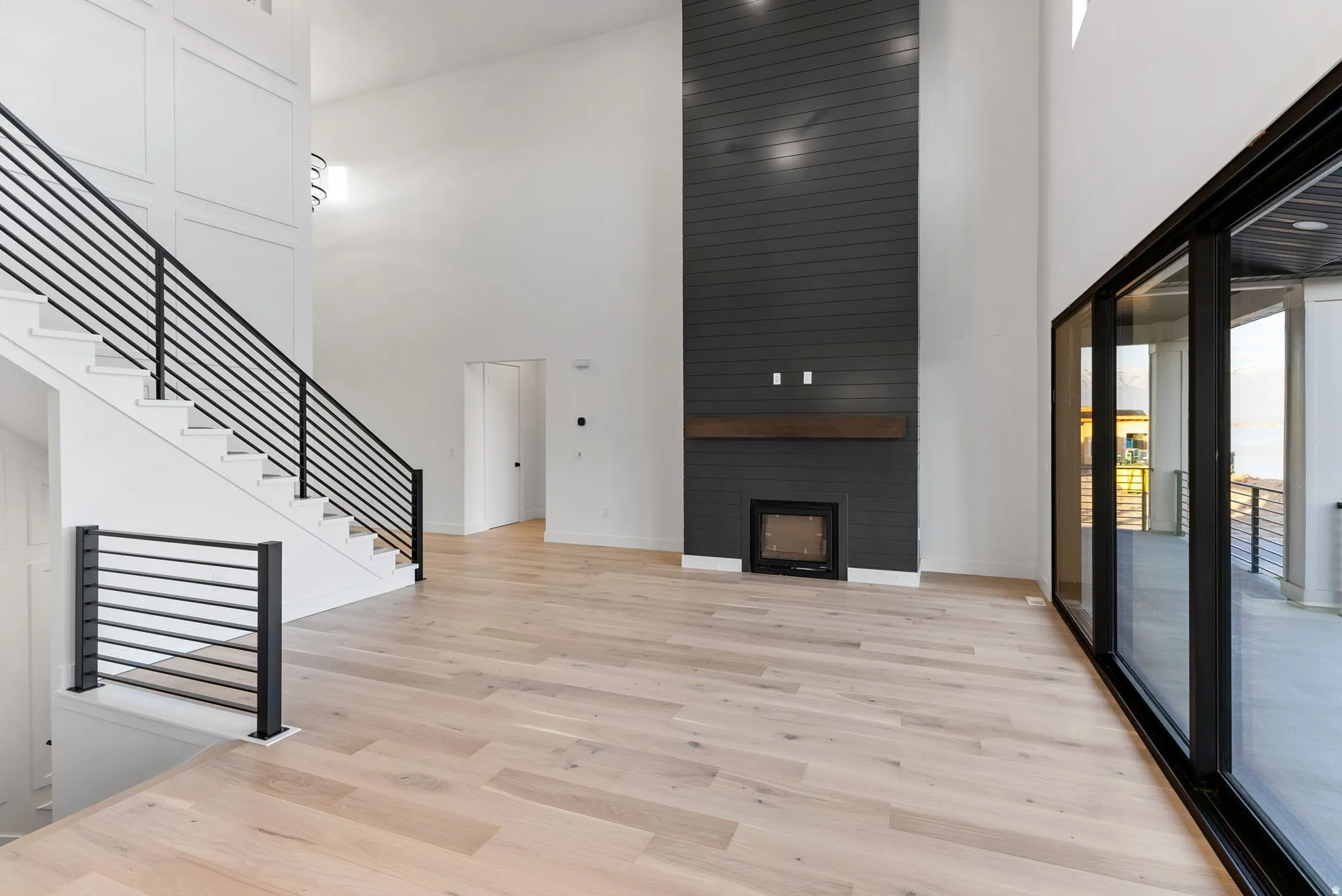 High ceilings, wood-finish flooring, a modern linear fireplace with a wood mantle, a full wall of sliding glass doors, and a staircase with contemporary black metal railings