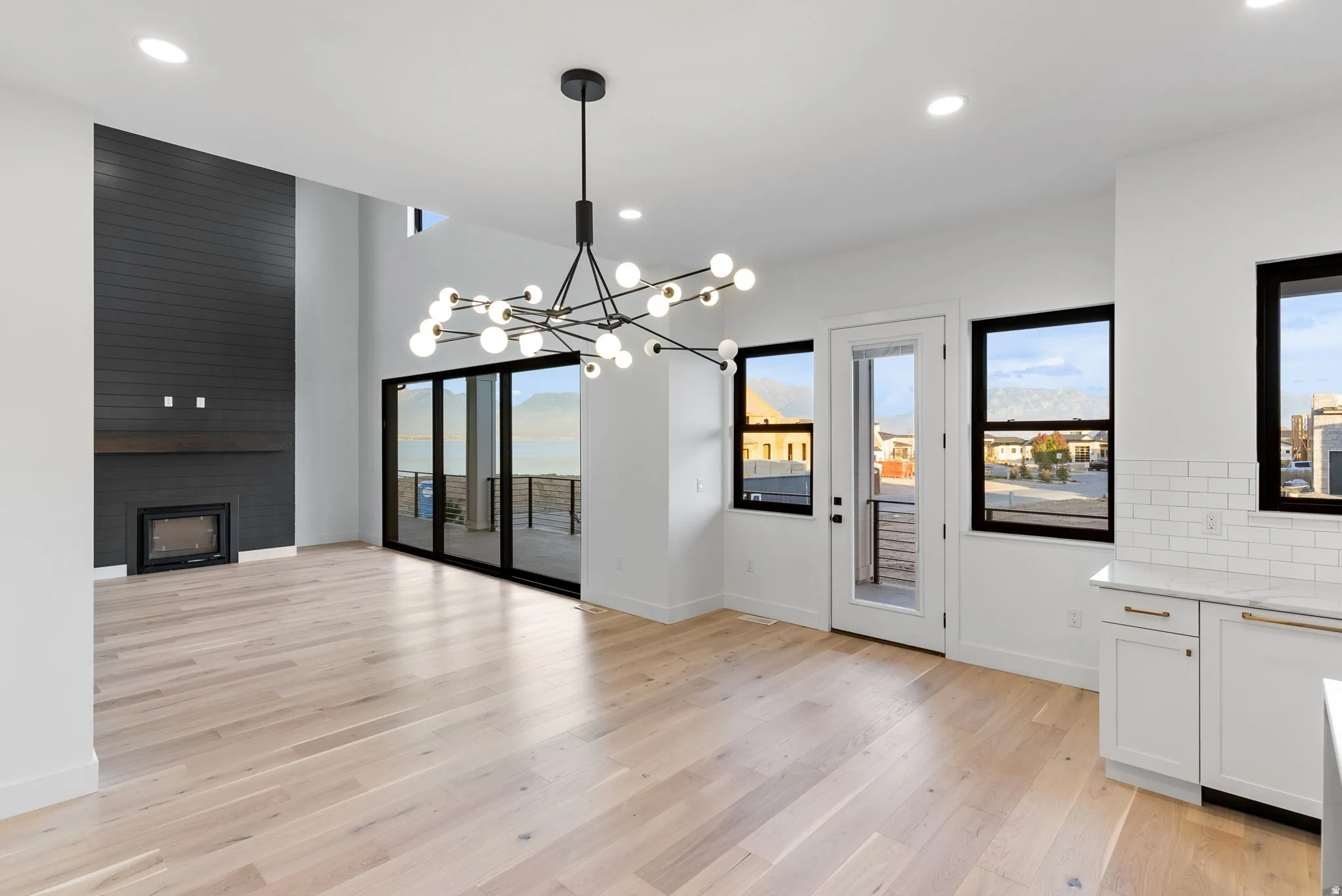 High ceilings, wood-finish flooring, a modern chandelier, a fireplace with a dark paneled accent wall, and sliding glass doors to the exterior