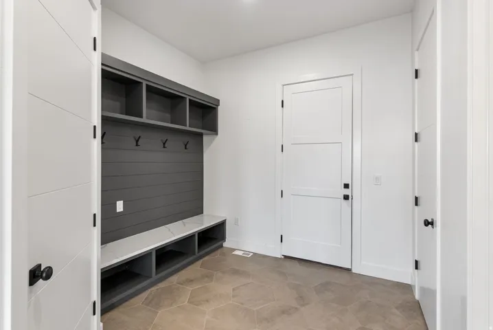Built-in mudroom storage with slat wall, open shelving, and integrated bench with a light-toned countertop, complemented by hexagonal floor tiles