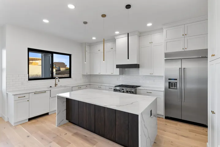 Gourmet kitchen featuring a waterfall island, white shaker-style cabinetry, stainless steel appliances, and wood-finish flooring