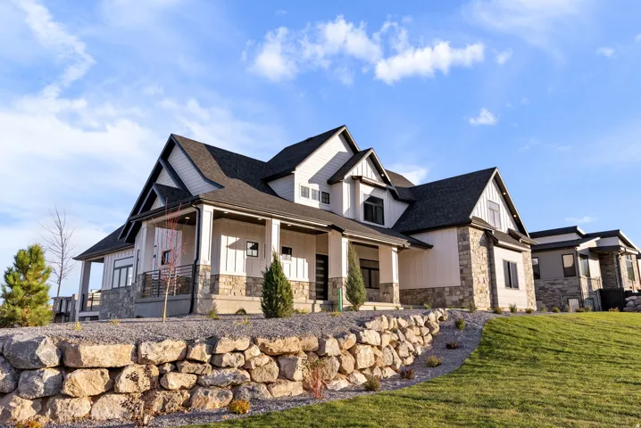 Modern farmhouse exterior with white vertical siding, dark trim, stone accents, covered front porch, and an asphalt shingle roof