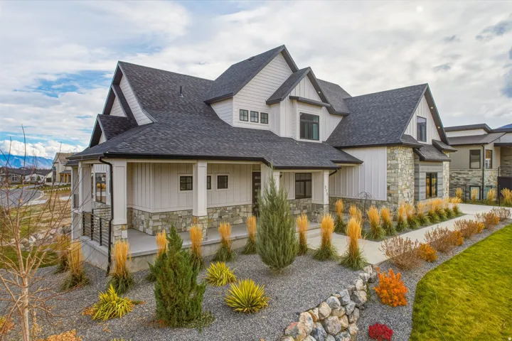 Exterior featuring a stone and siding facade, multiple gables, a covered porch with square columns, dark-framed windows, and a landscaped yard