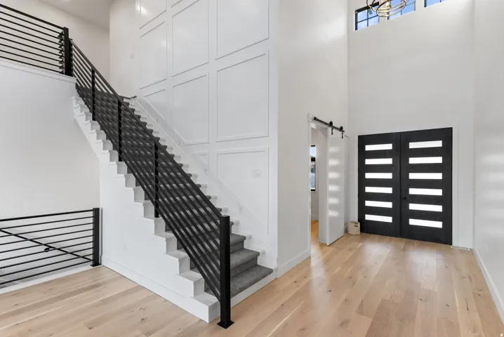 Vaulted entry with light wood-finish flooring, black double entry doors, panel accent wall, and a staircase with black railings