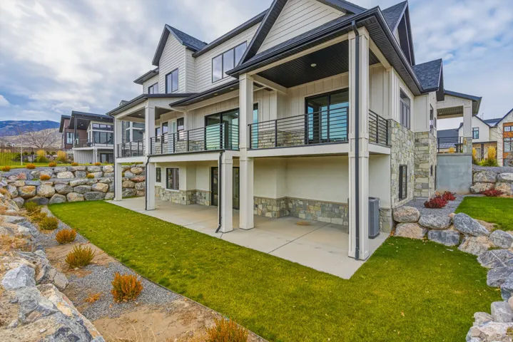 Multi-level exterior featuring white siding, stone accents, black-framed windows, multiple balconies with dark railings, and a lower-level patio