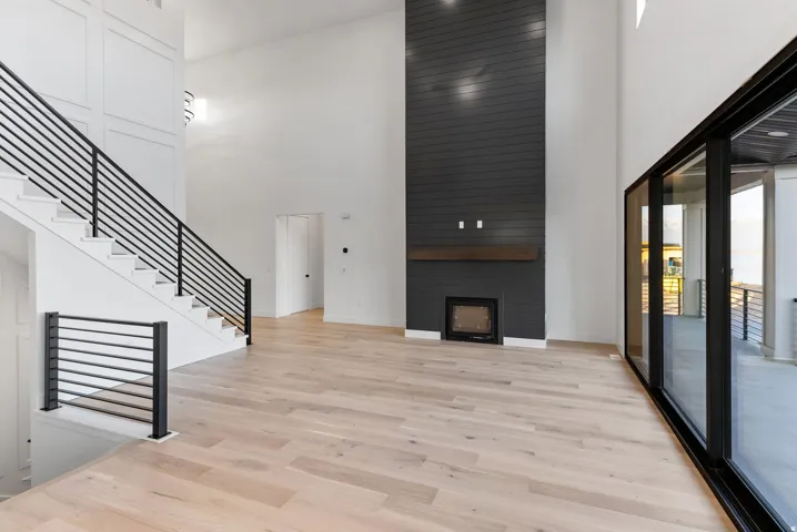 High ceilings, wood-finish flooring, a modern linear fireplace with a wood mantle, a full wall of sliding glass doors, and a staircase with contemporary black metal railings