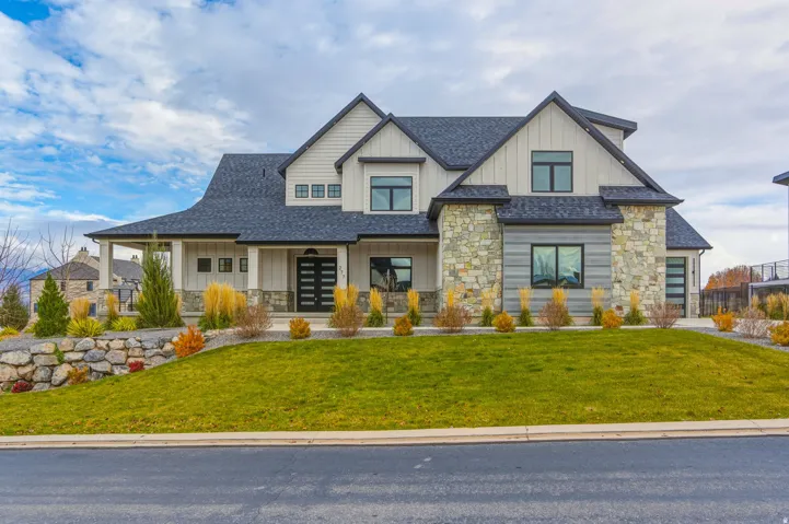 Modern farmhouse exterior featuring board and batten siding, stone accents, a covered front porch, a dark shingled roof, and a multi-panel front door