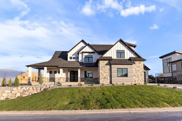 Modern farmhouse exterior featuring board and batten siding, stone accents, a covered entry, dark-framed windows, and a multi-pane front door
