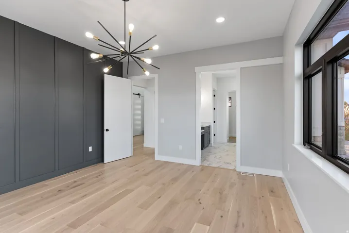 Light wood-finish flooring, accent wall with vertical paneling, modern sputnik chandelier, large window with dark trim, and a pocket door opening to a tiled area