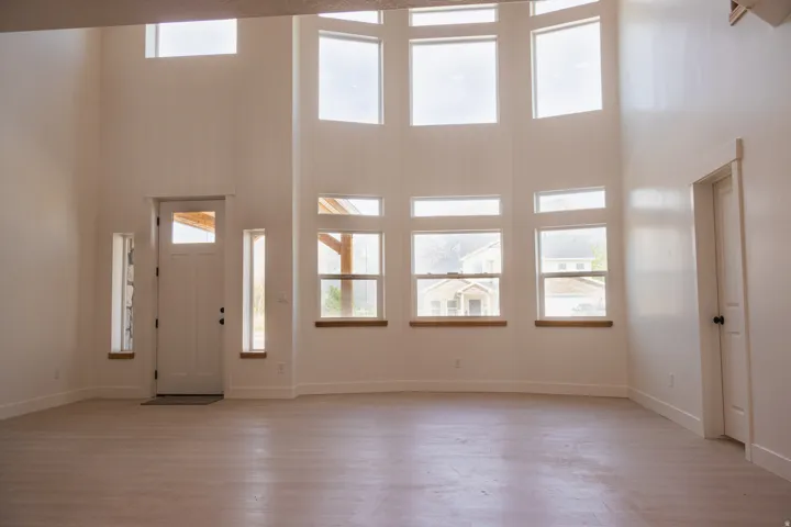 Vaulted ceilings, expansive window wall, wood-finish flooring, white paneled entry door, and white trim throughout
